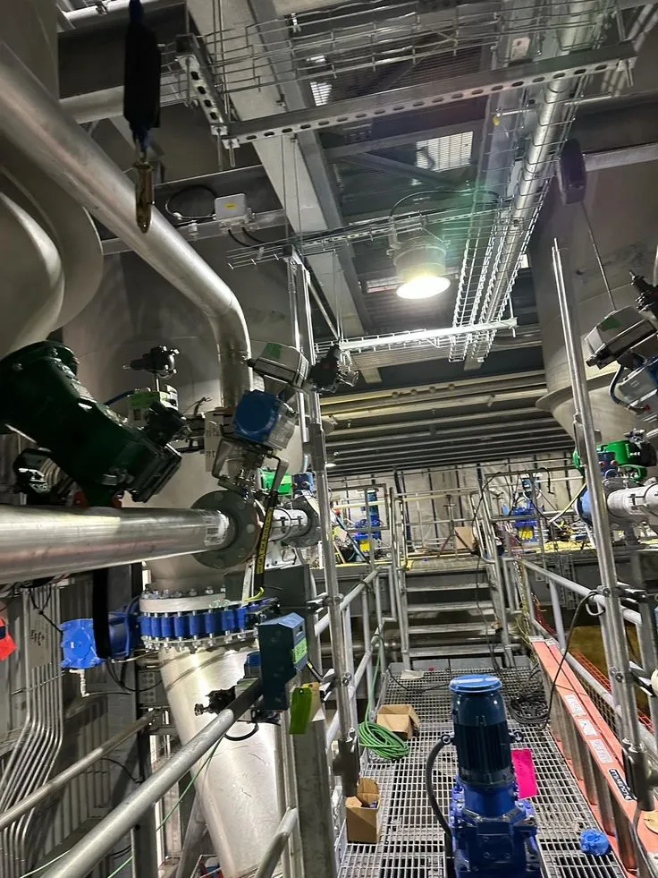 Industrial piping system with valves, pumps, and stainless steel pipelines inside a mechanical plant room.